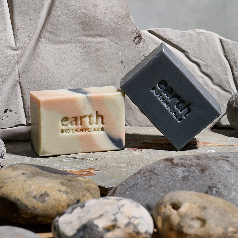 Two bars of Earth Botanicals soap on a stone surface with rocks in the foreground.
