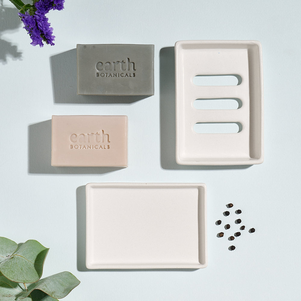 Two soaps from the Air Collection on a light grey background with eucalyptus leaf, black pepper and a jesmonite soap dish with tray
