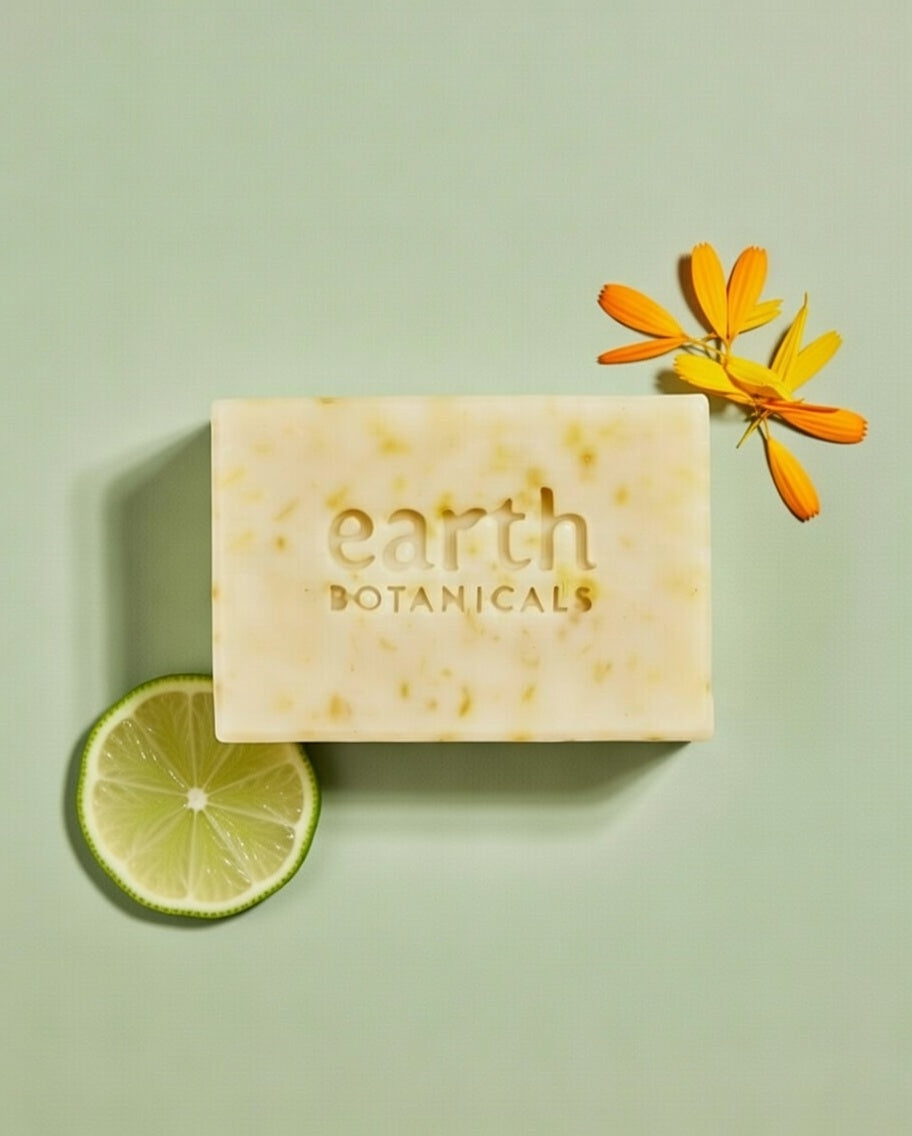 Bar of soap with 'earth botanics' branding on a light green background with a lime wedge and flower.